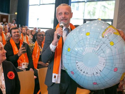 Mann mit einer großen Weltkugel unter dem Arm spricht vor einer Versammlung